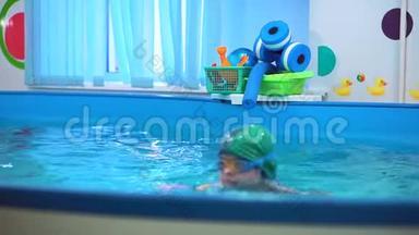游泳池里那个戴泳镜的男孩跳水了。 他从底部得到玩具，教练训练他潜水。